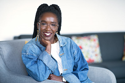 Ms. Nwamaka Agbo, smiling brightly, wearing glasses and jean jacket, with gold jewelry