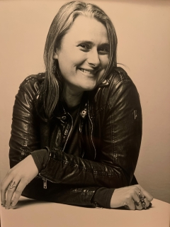 Sepia toned Lauren Lambert, smiling, arms crossed wearing a leather coat and lots of cool rings
